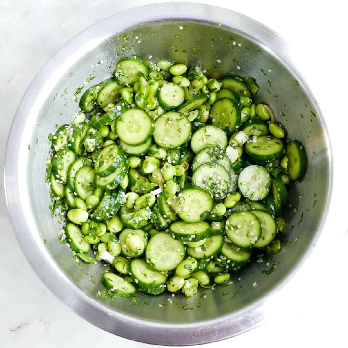 Ingredients and dressing for edamame cucumber salad mixed together in a bowl.
