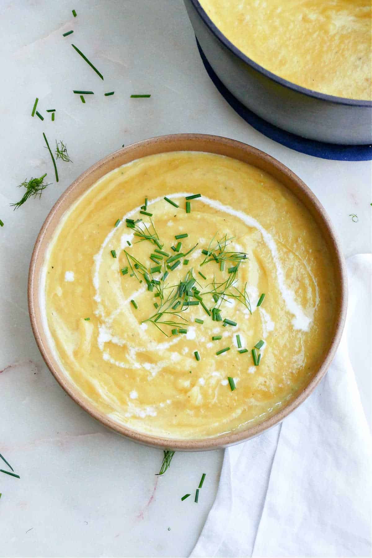 Fennel leek soup topped with herbs in a tan colored bowl. 