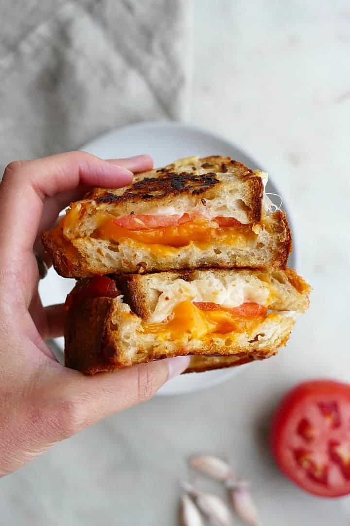 Holding two halves of a Garlic Bread Grilled Cheese with Heirloom Tomato.
