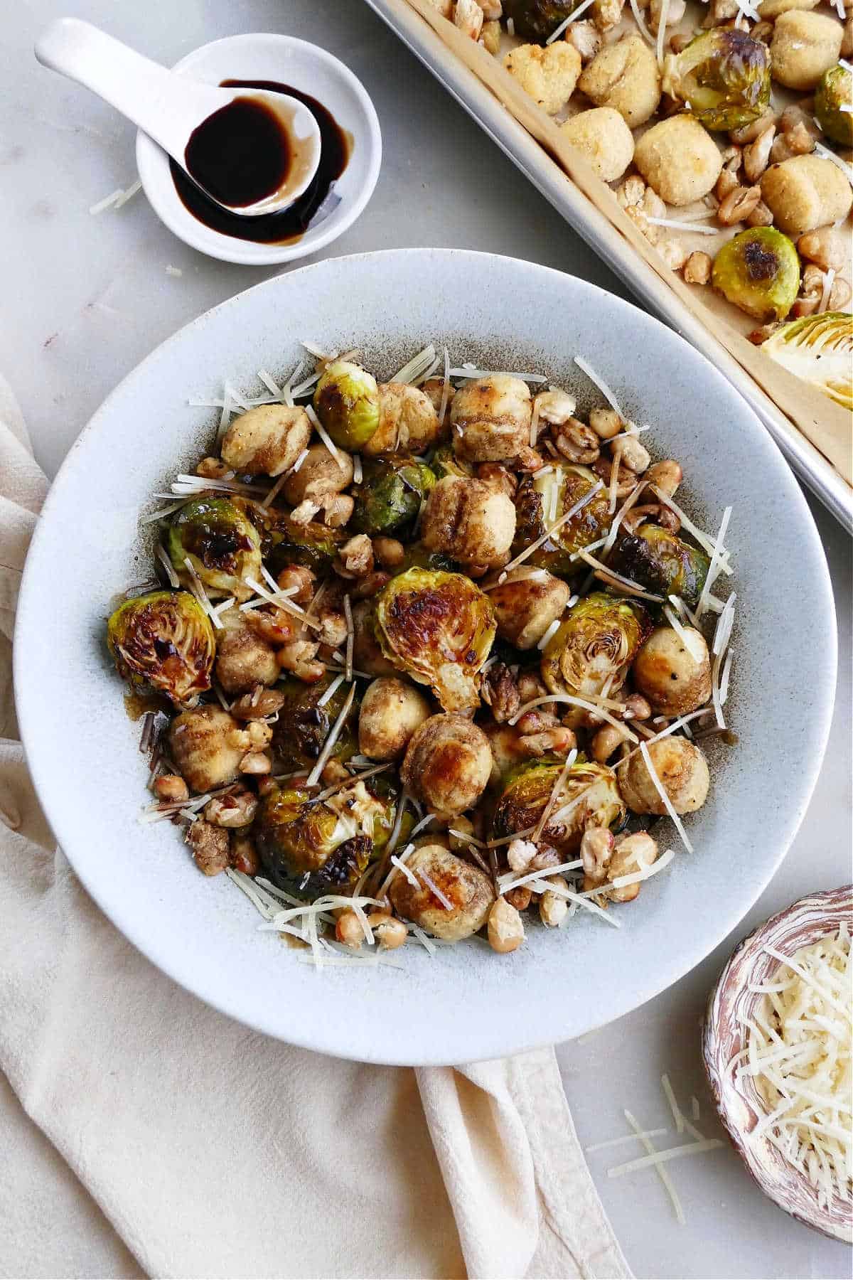 Sheet Pan Gnocchi and Brussels Sprouts in a large white bowl next to parmesan cheese.