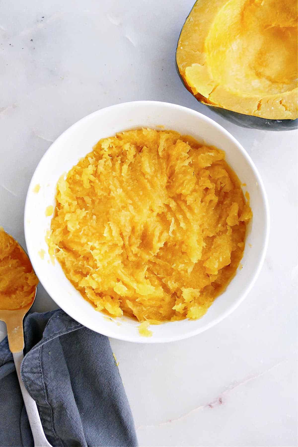 A bowl of Instant Pot acorn squash next to an acorn squash halve. 