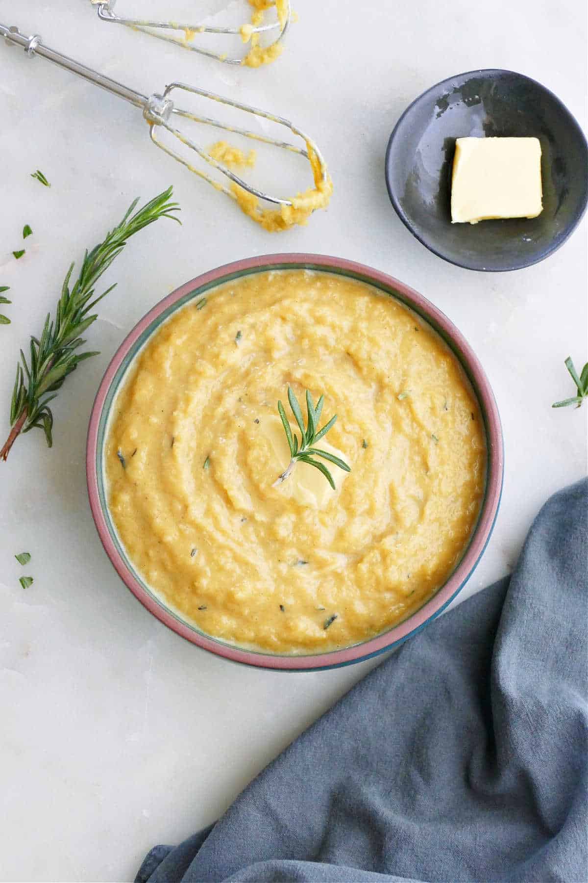 A plate of mashed acorn squash with maple and topped with rosemary next to a bowl of butter. 