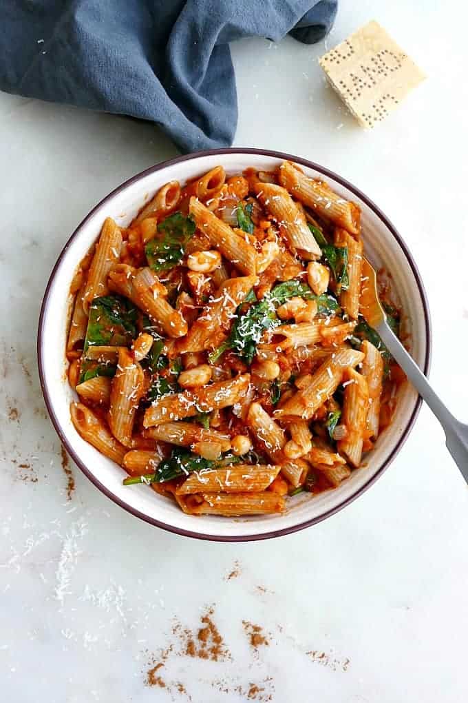 Pumpkin tomato pasta in a white bowl next to a blue kitchen towel.