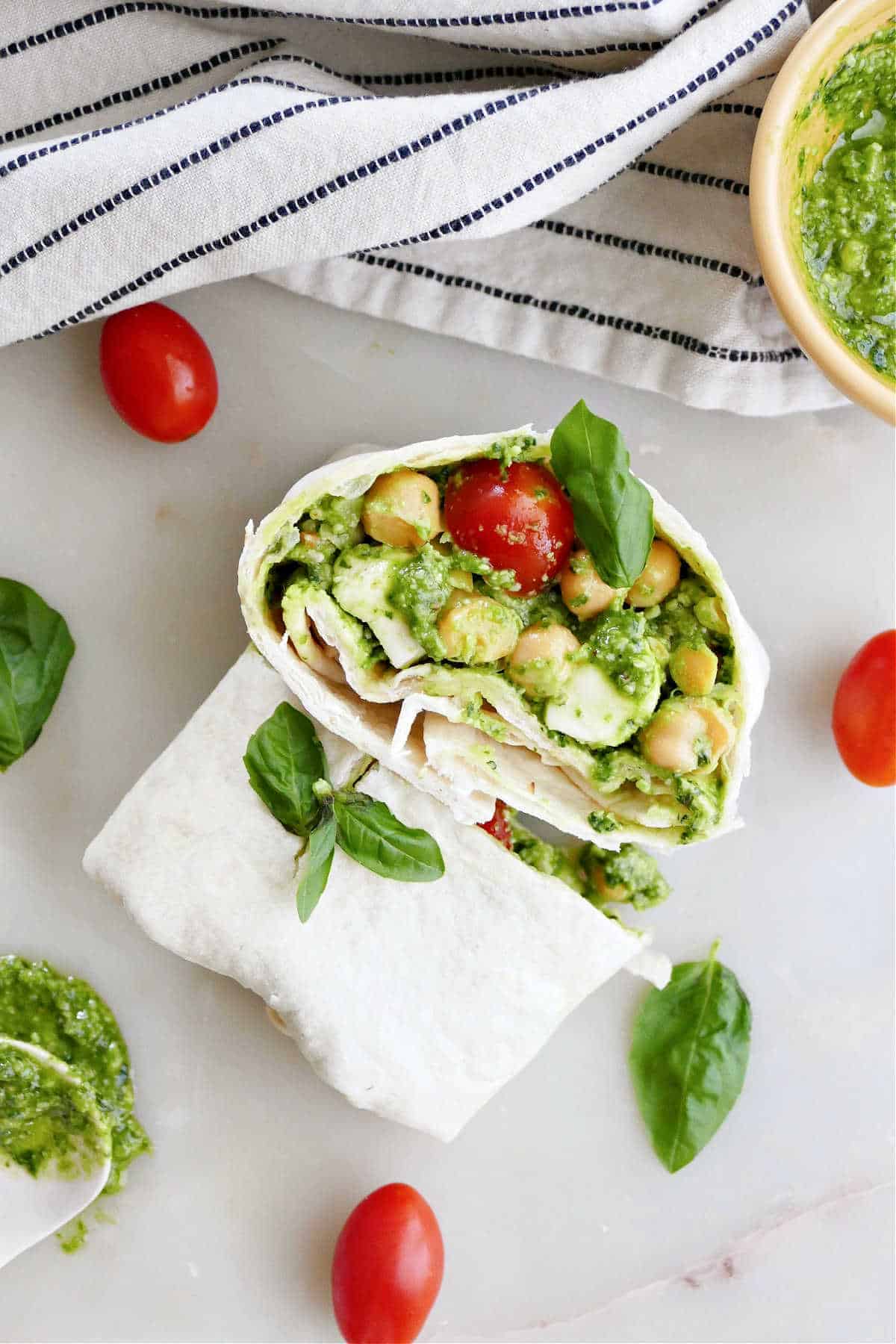 A pesto chickpea wrap sliced open stacked on each other with garnish and tomatoes.