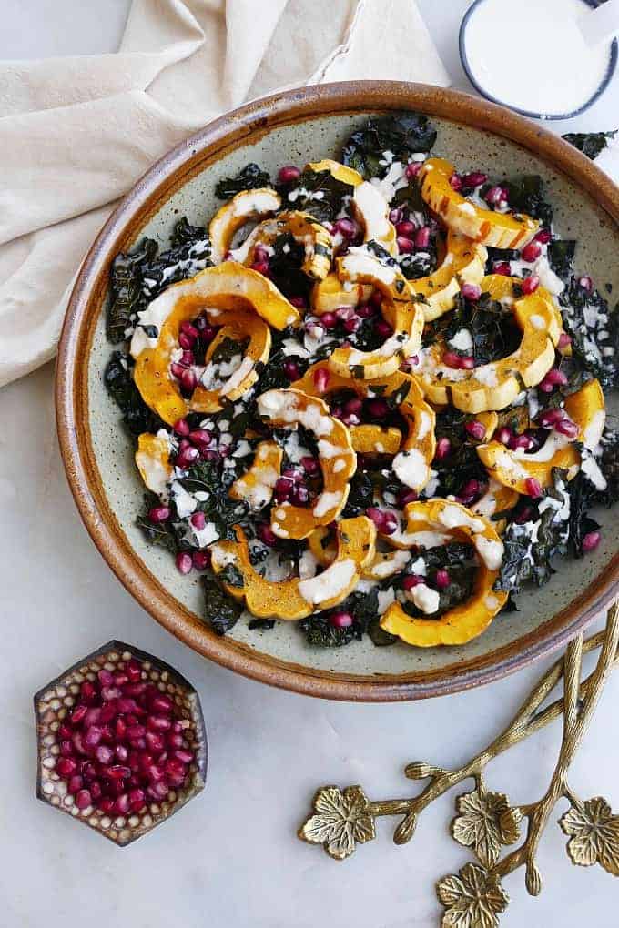 Roasted Delicata Squash and Kale with Lemon Tahini topped with pomegranate seeds next to a kitchen towel. 