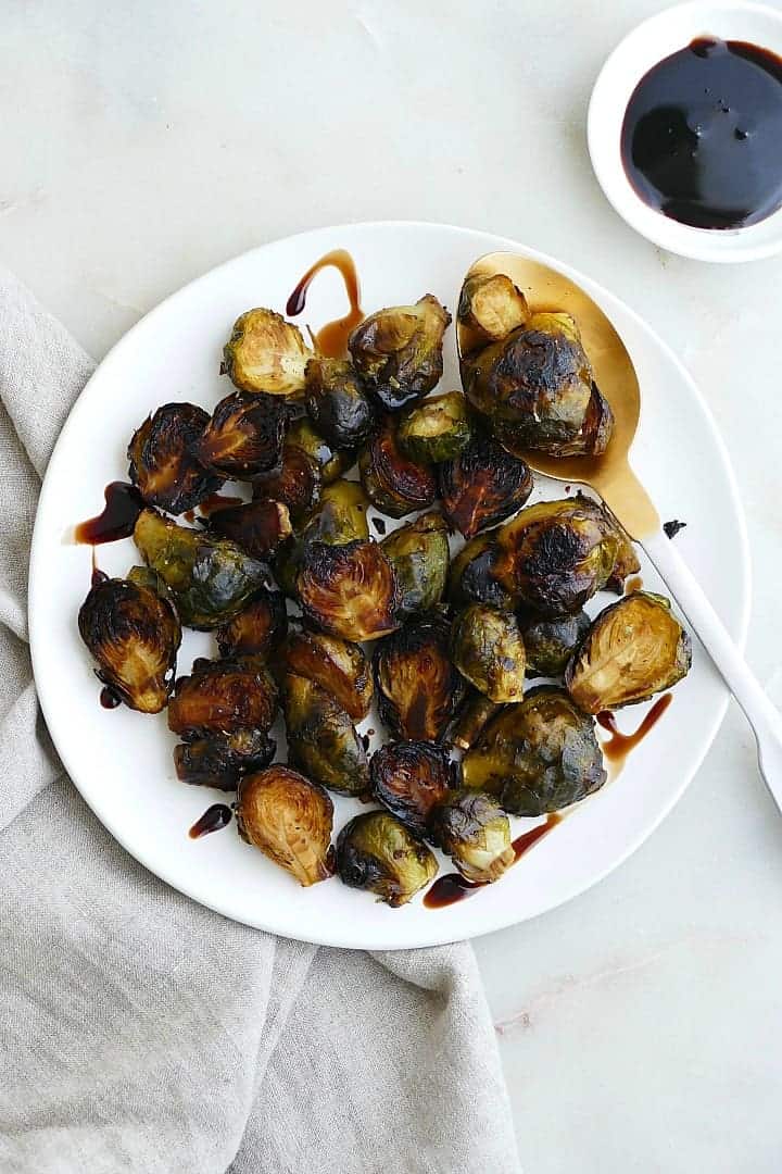 Roasted Frozen Brussels Sprouts on a white plate with a spoon tossed in balsamic.