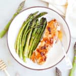 Honey glazed salmon and roasted asparagus on a plate with a fork.