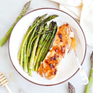Honey glazed salmon and roasted asparagus on a plate with a fork.