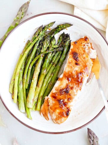 Honey glazed salmon and roasted asparagus on a plate with a fork.