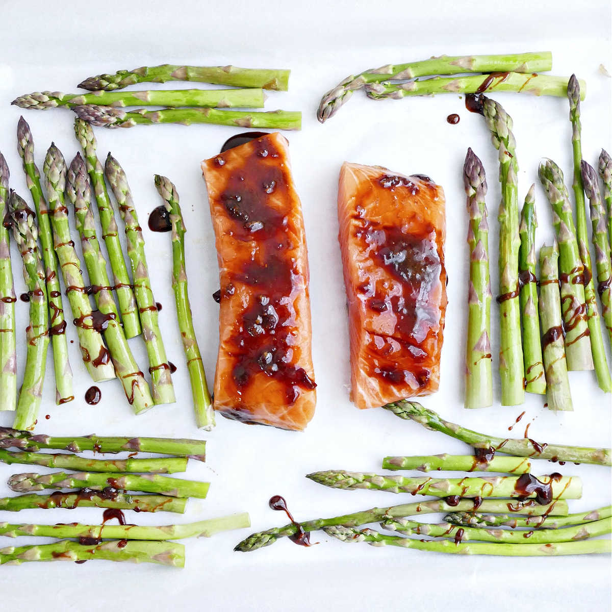 Salmon and asparagus on a sheet pan brushed with honey soy glaze.