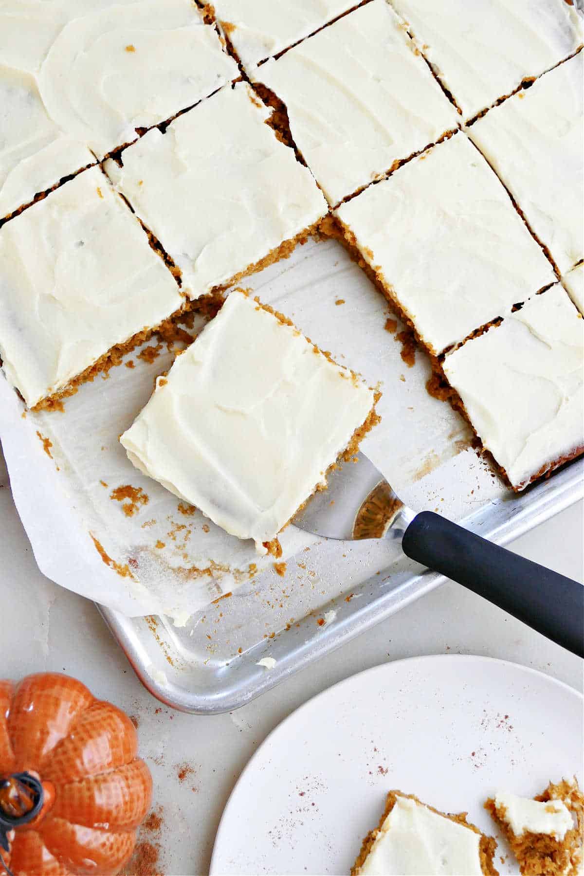 A sheet pan of frosted pumpkin bars with a spatula lifting one out. 