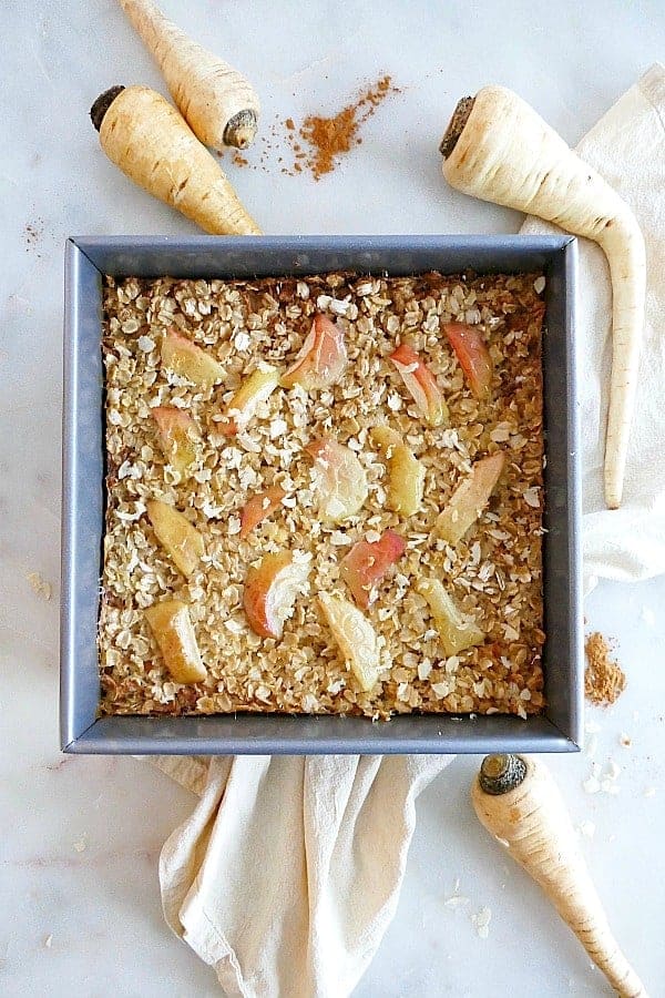 Parsnip apple baked oatmeal in a square baking dish surrounded by fresh parsnips.