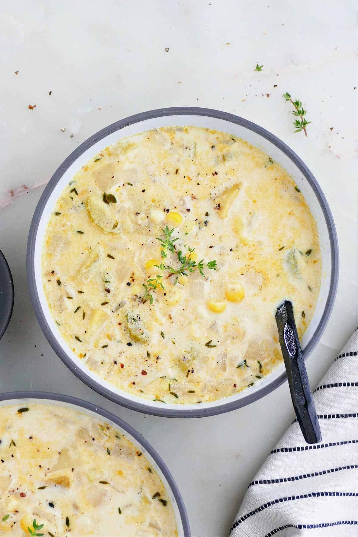 Two bowls of sweet corn soul next to a striped kitchen towel. 