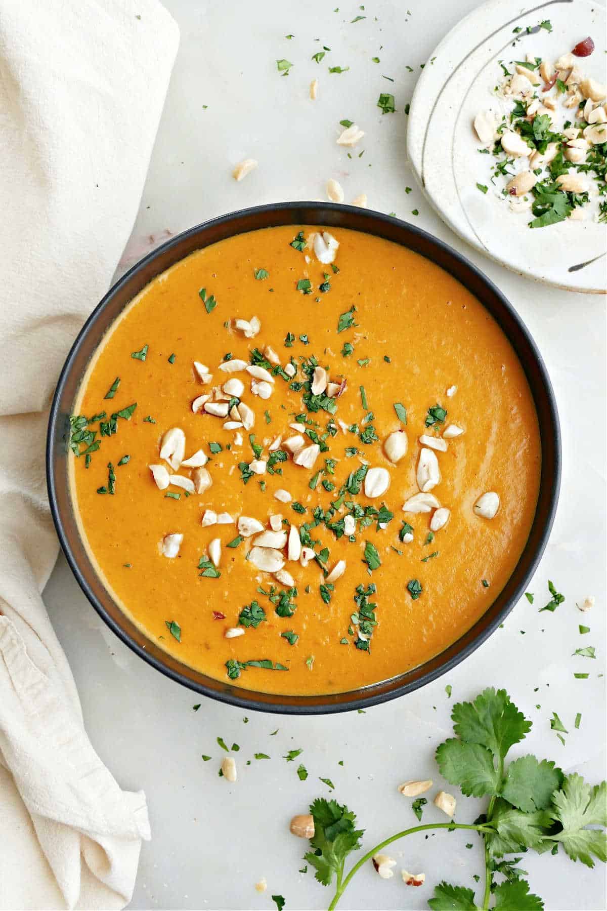 A bowl of sweet potato and red pepper soup sprinkled with cilantro and peanuts.