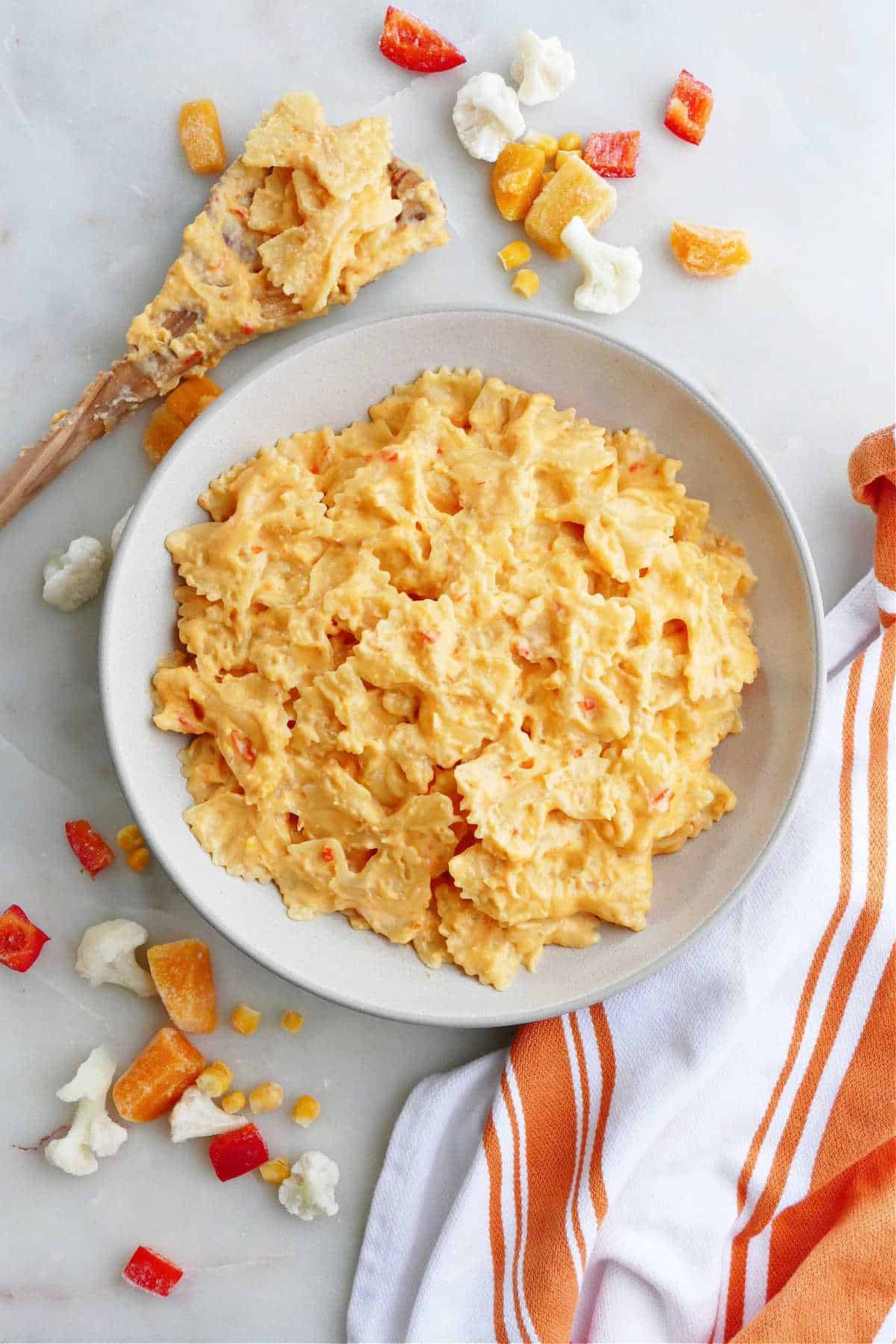 Bowl of hidden veggie mac and cheese next to a wooden spoon covered in mac and cheese.