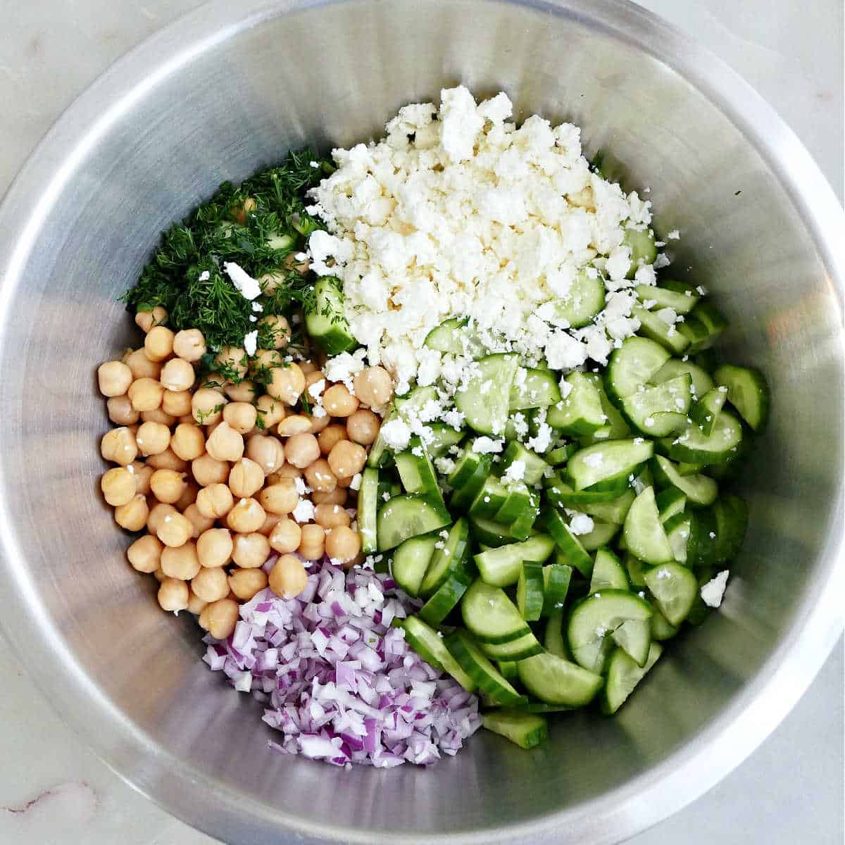 Chickpeas, herbs, feta cheese, cucumbers, and red onion in a mixing bowl.