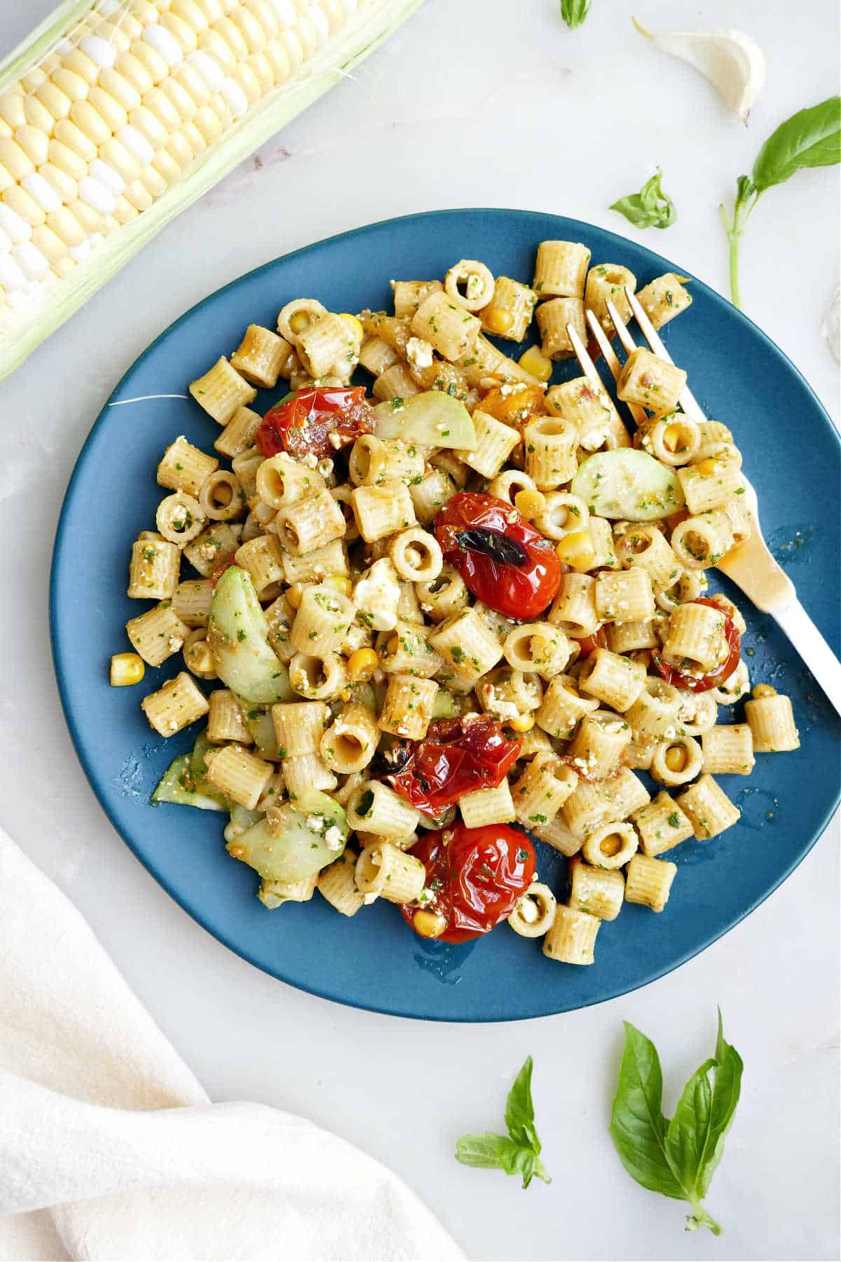 Summer pasta salad with basil vinaigrette on a blue plate with a fork.