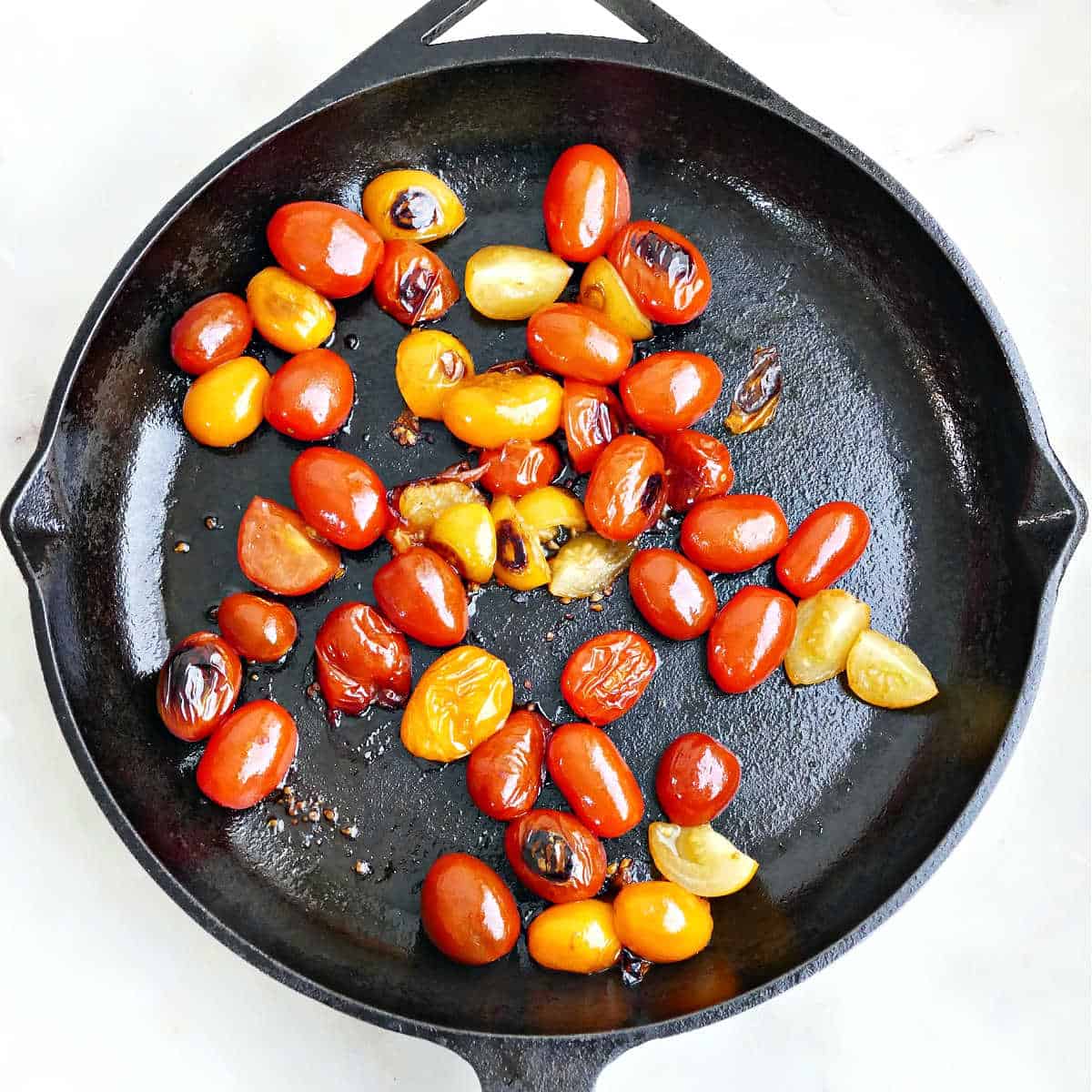 Blistered cherry tomatoes cooking in a cast iron skillet.