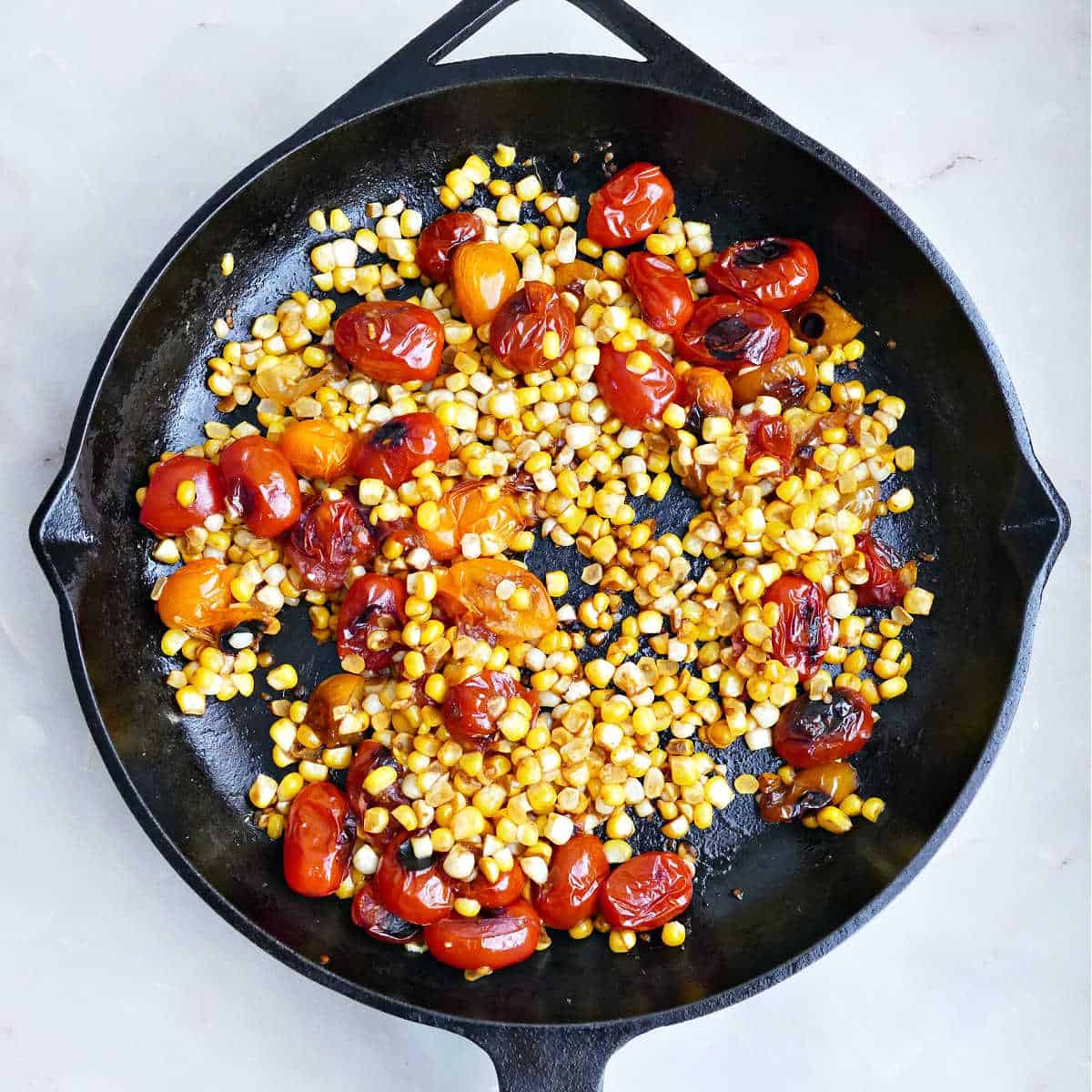 Blistered corn and cherry tomatoes cooking in a cast iron skillet.