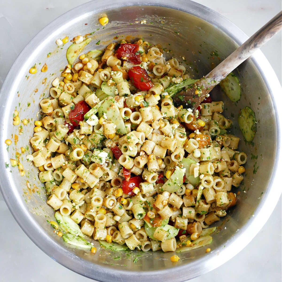 Ditalini pasta salad tossed with basil dressing in a bowl with a wooden spoon.