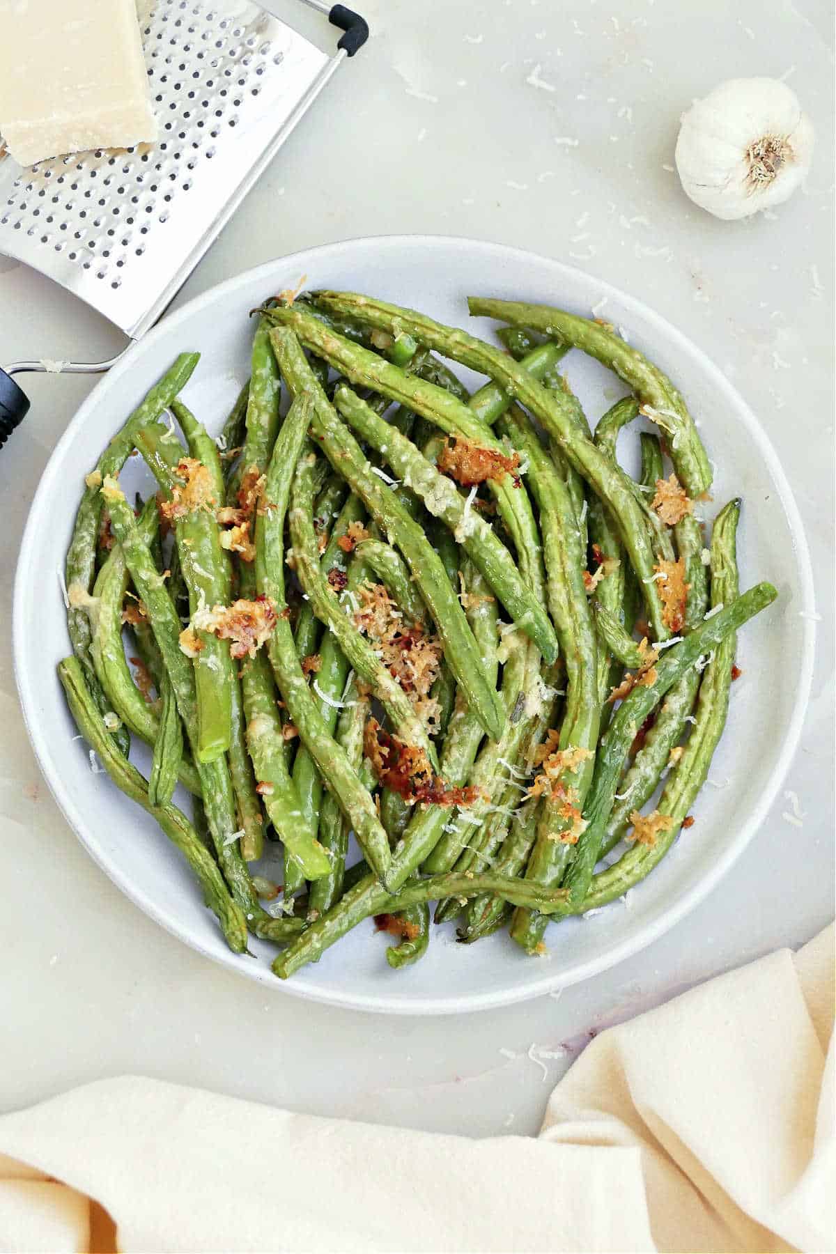 Roasted garlic green beans on a serving plate next to a napkin and ingredients.
