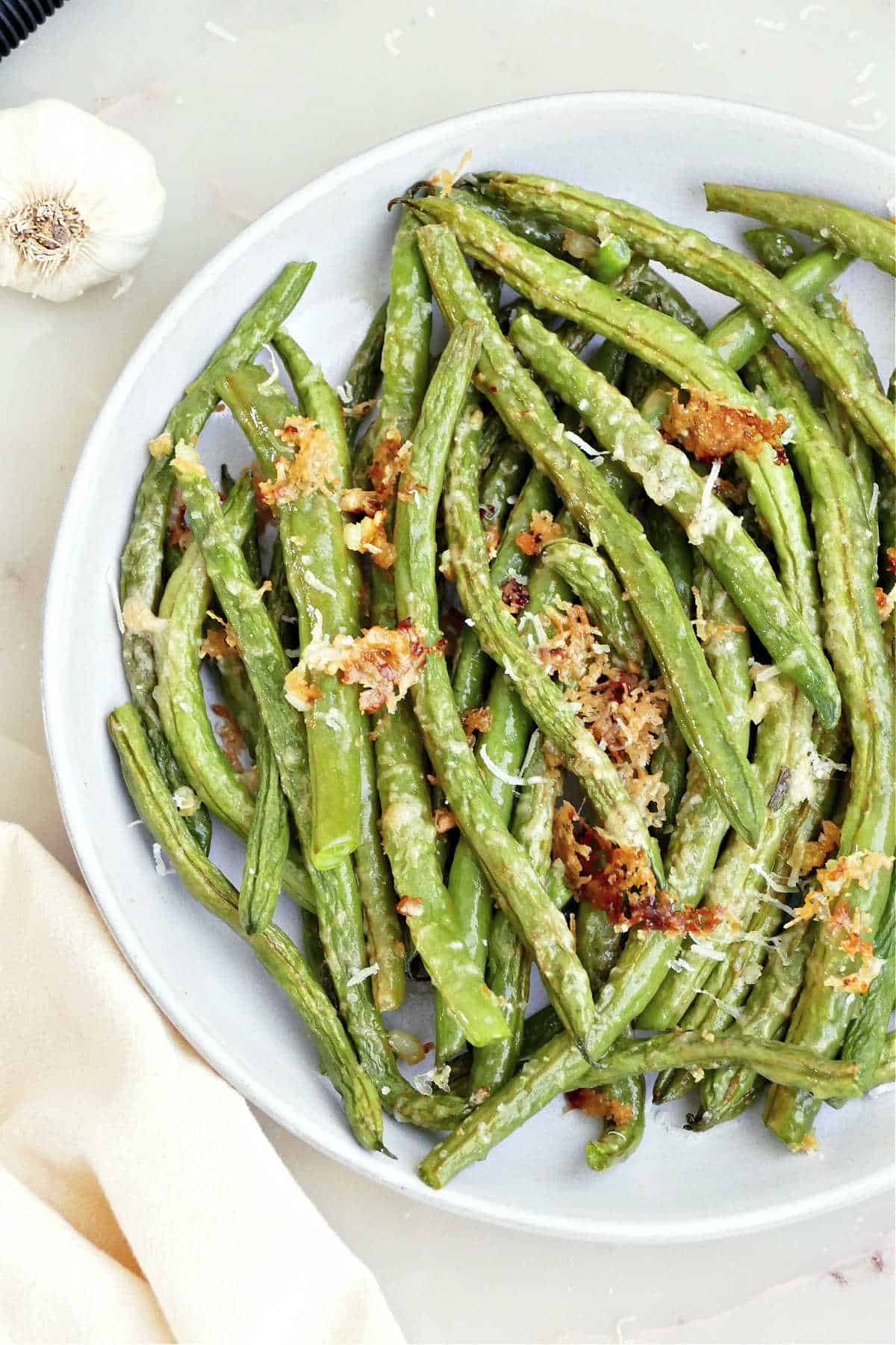 Green beans topped with crispy garlic and parmesan on a plate.