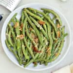 Roasted garlic green beans on a serving plate next to a napkin and ingredients.