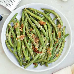 Roasted garlic green beans on a serving plate next to a napkin and ingredients.