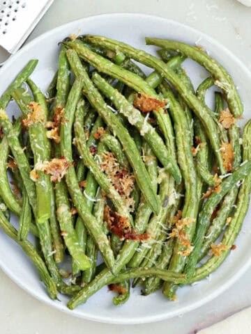 Roasted garlic green beans on a serving plate next to a napkin and ingredients.