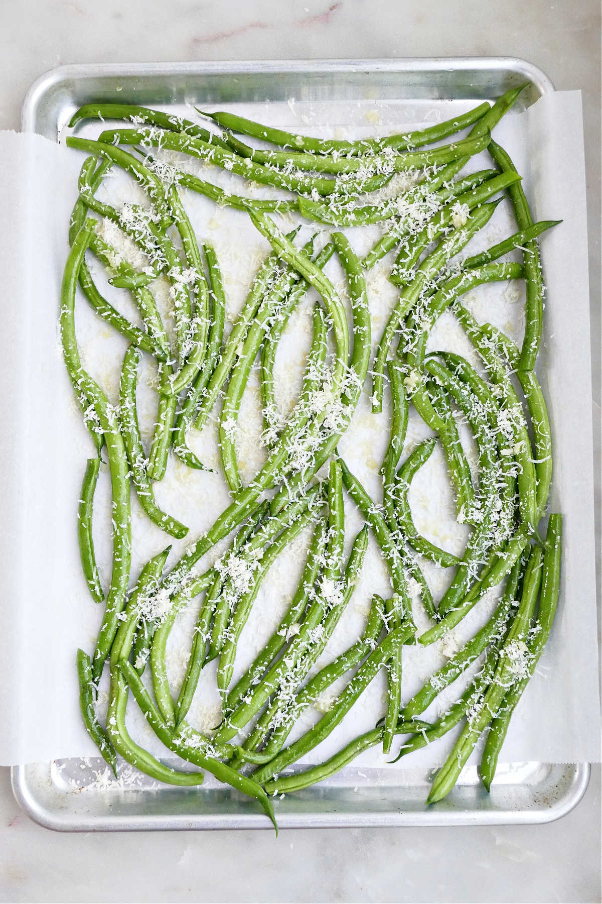 Green beans tossed in garlic and parmesan on a lined baking sheet before roasting.