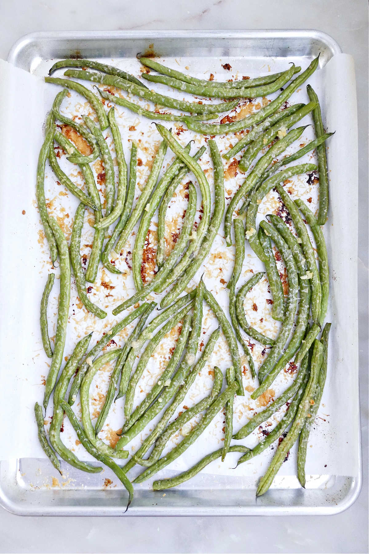 Roasted green beans with garlic and cheese on a lined baking sheet.