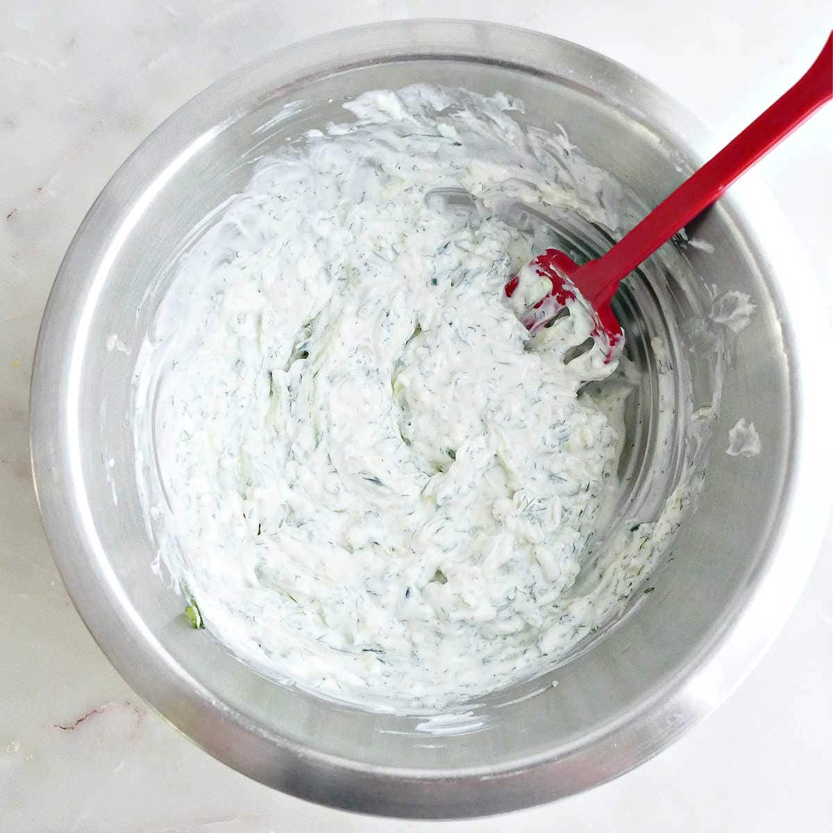 Cucumber yogurt sauce stirred together in a bowl with a silicone fork.