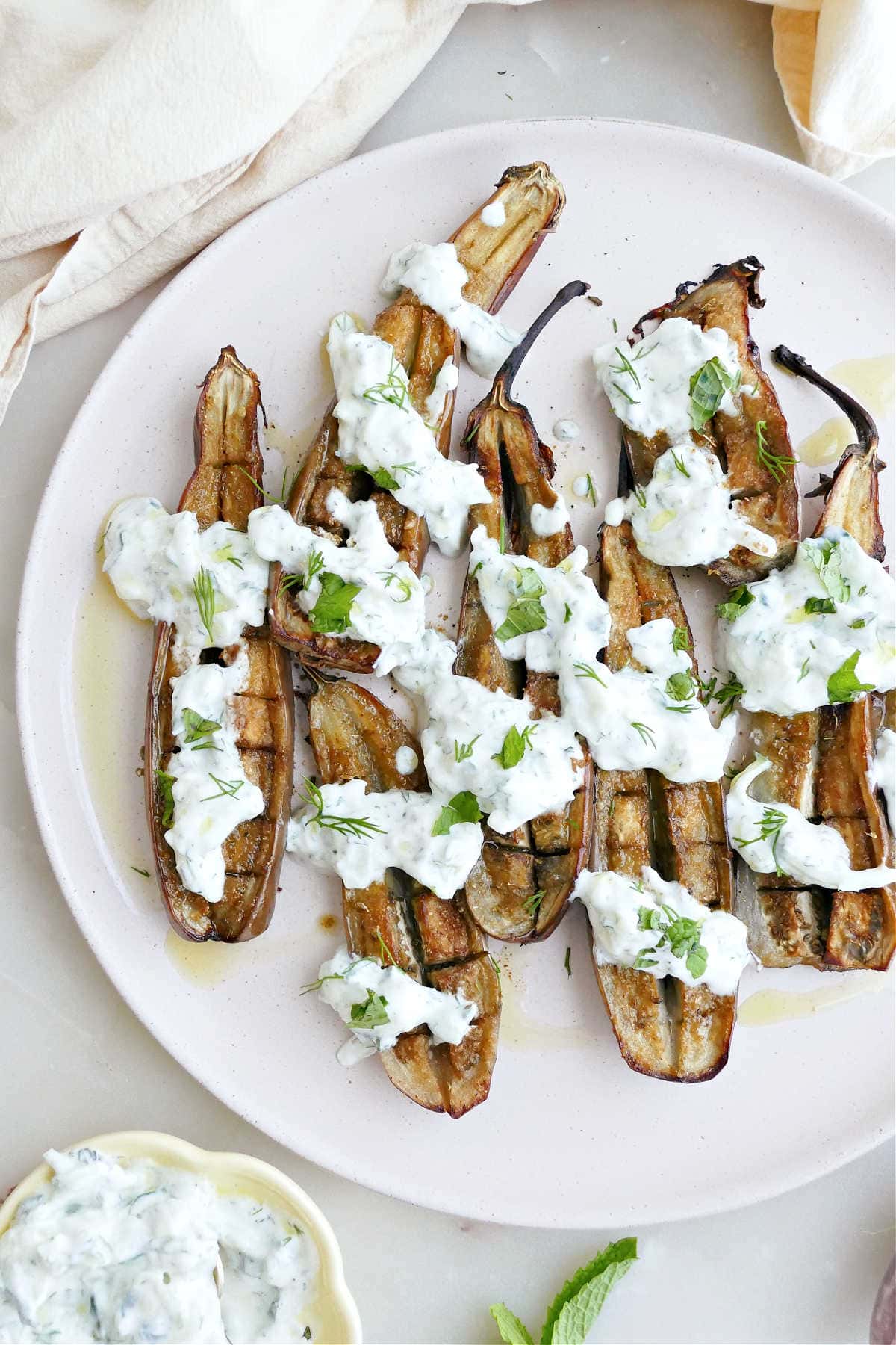 Roasted mini eggplant halves with cucumber yogurt sauce on a plate.