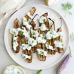 Baby eggplants with cucumber sauce on a plate next to napkins and ingredients.