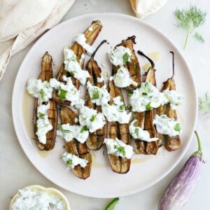 Baby eggplants with cucumber sauce on a plate next to napkins and ingredients.