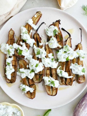 Baby eggplants with cucumber sauce on a plate next to napkins and ingredients.
