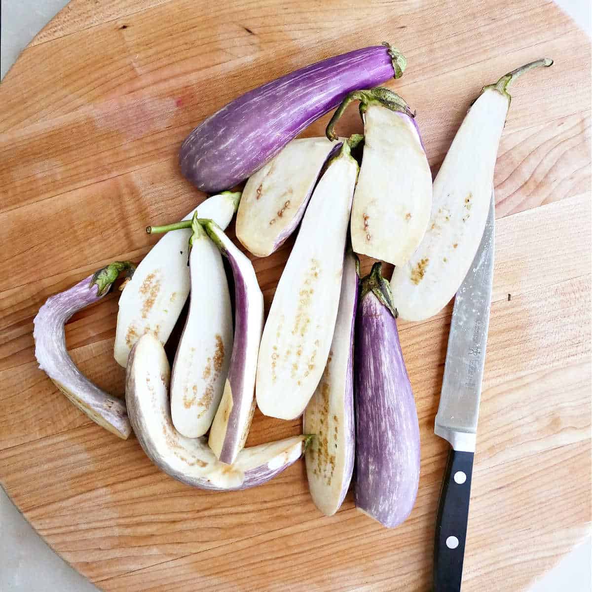 Mini eggplants sliced in half lengthwise on a cutting board.