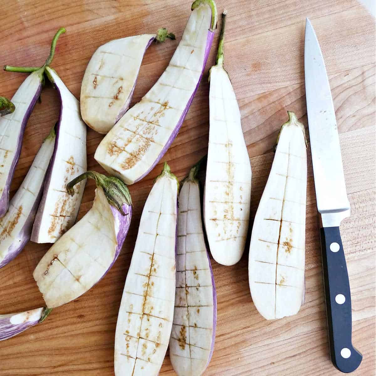 Eggplant halves scored with a knife on a cutting board.
