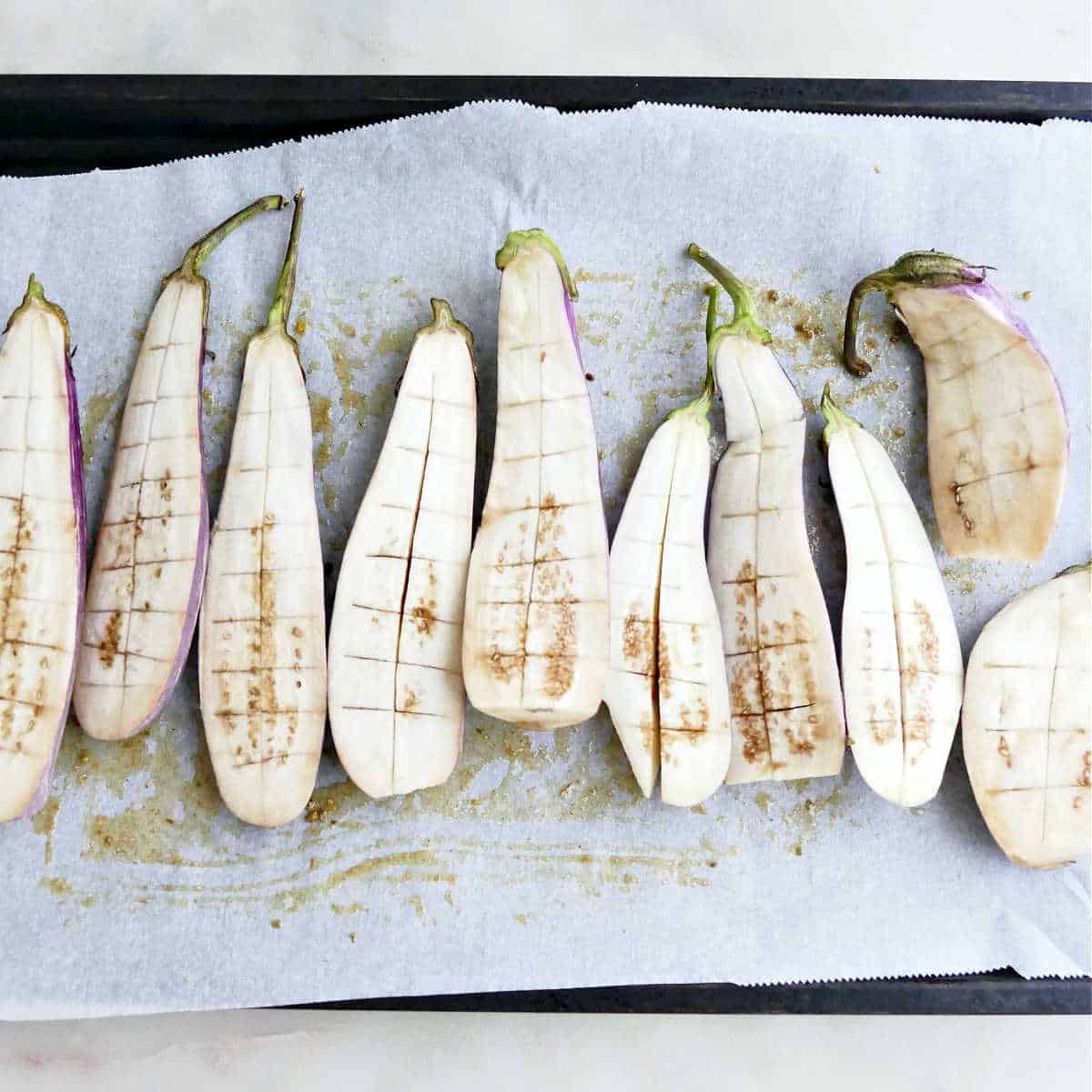Eggplant halves on a lined baking sheet before being brushed with oil.
