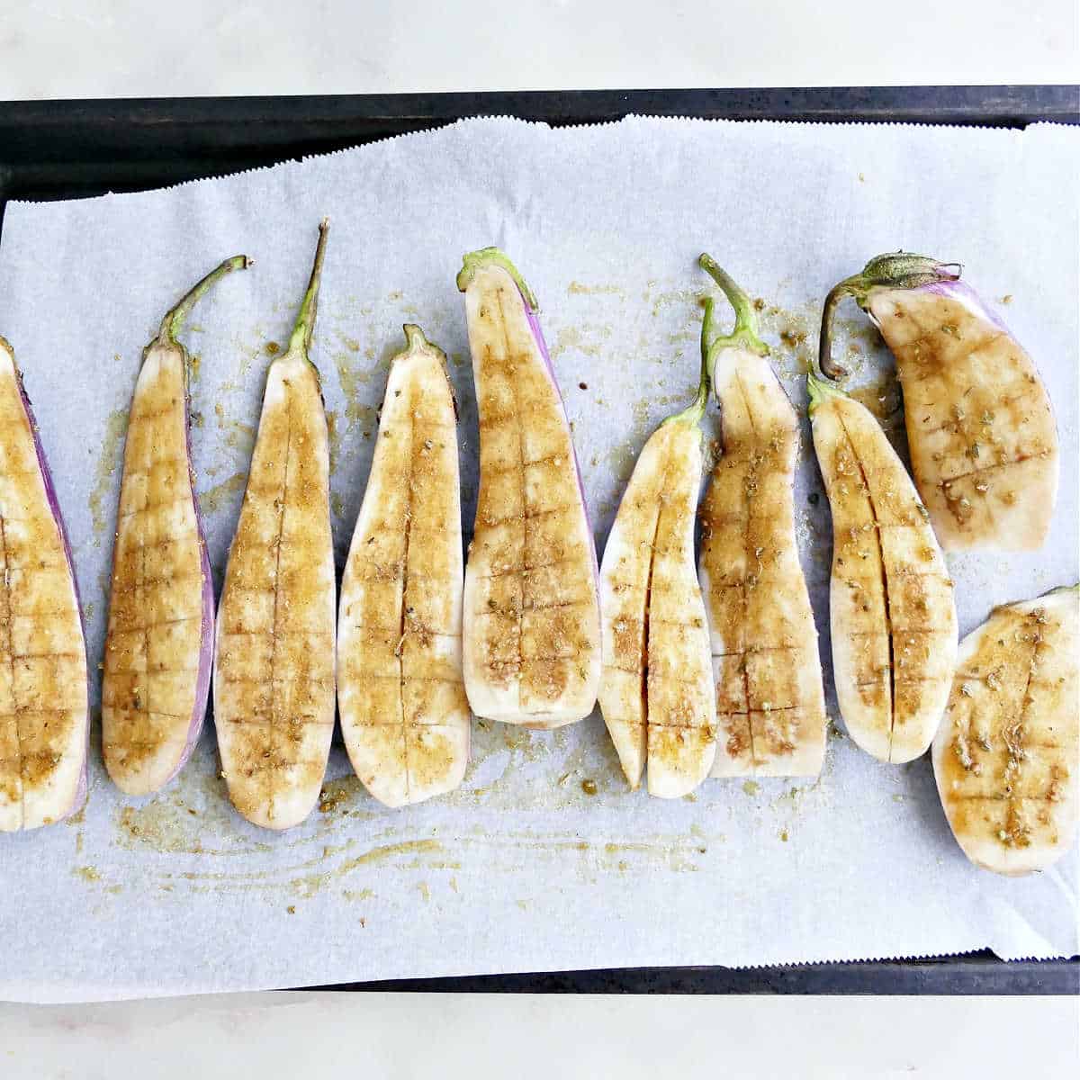 Scored eggplant halves on a baking sheet brushed with oil and spices.
