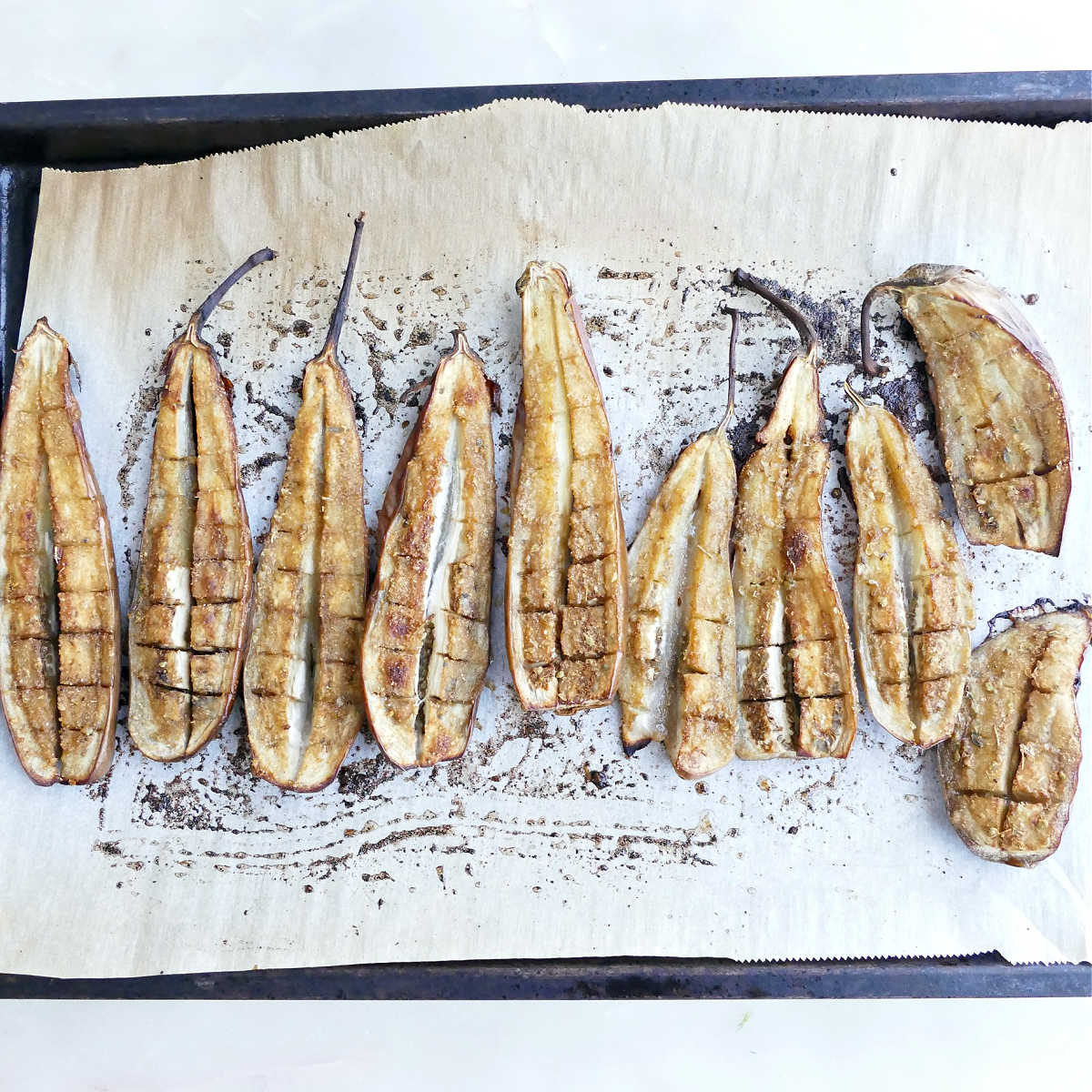 Baby eggplants on a lined baking sheet after being roasted in the oven.
