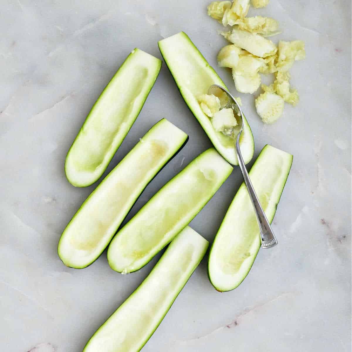 Zucchini boats with seeds being removed on a counter.