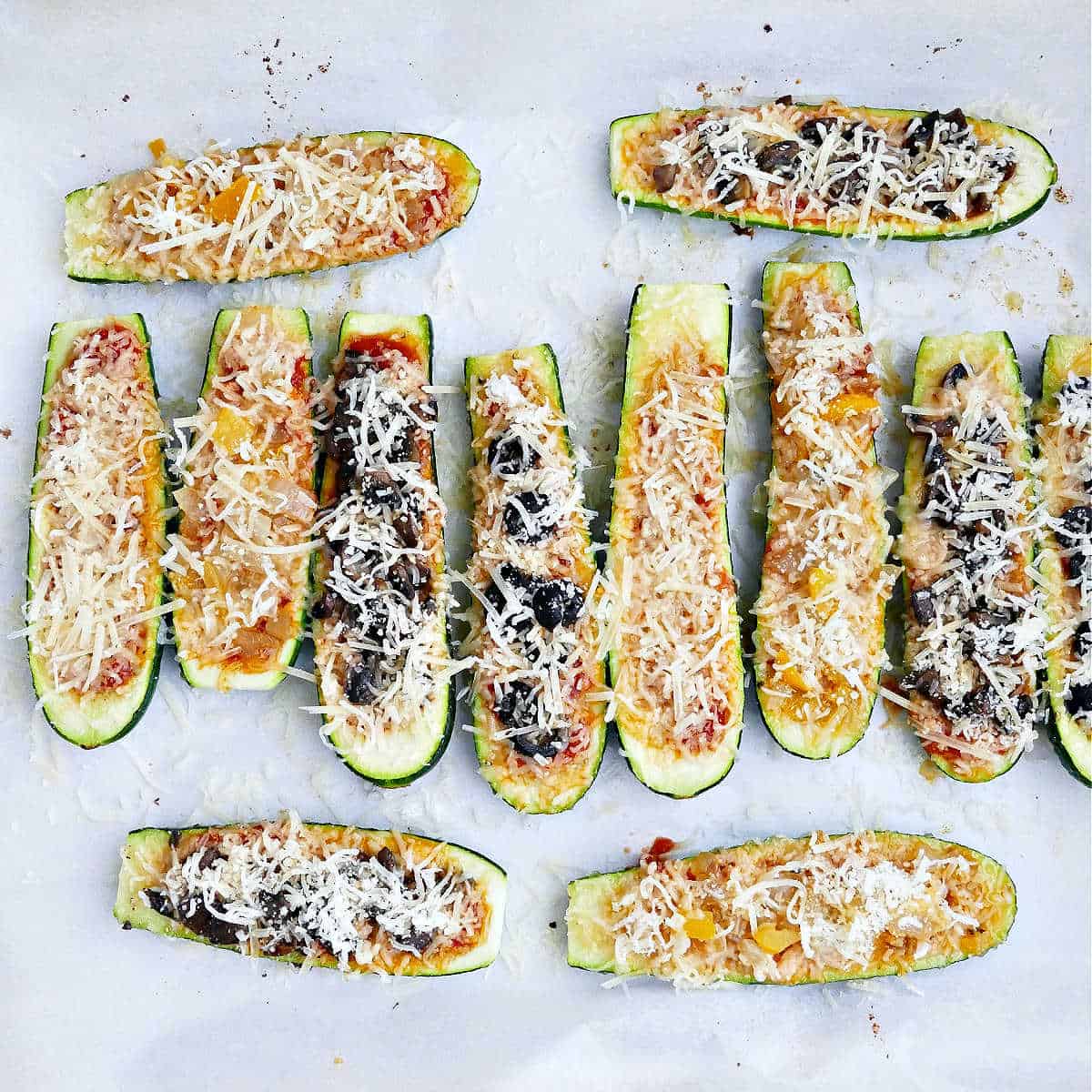 Zucchini boats stuffed with sauce, cheese, and various toppings before being baked.