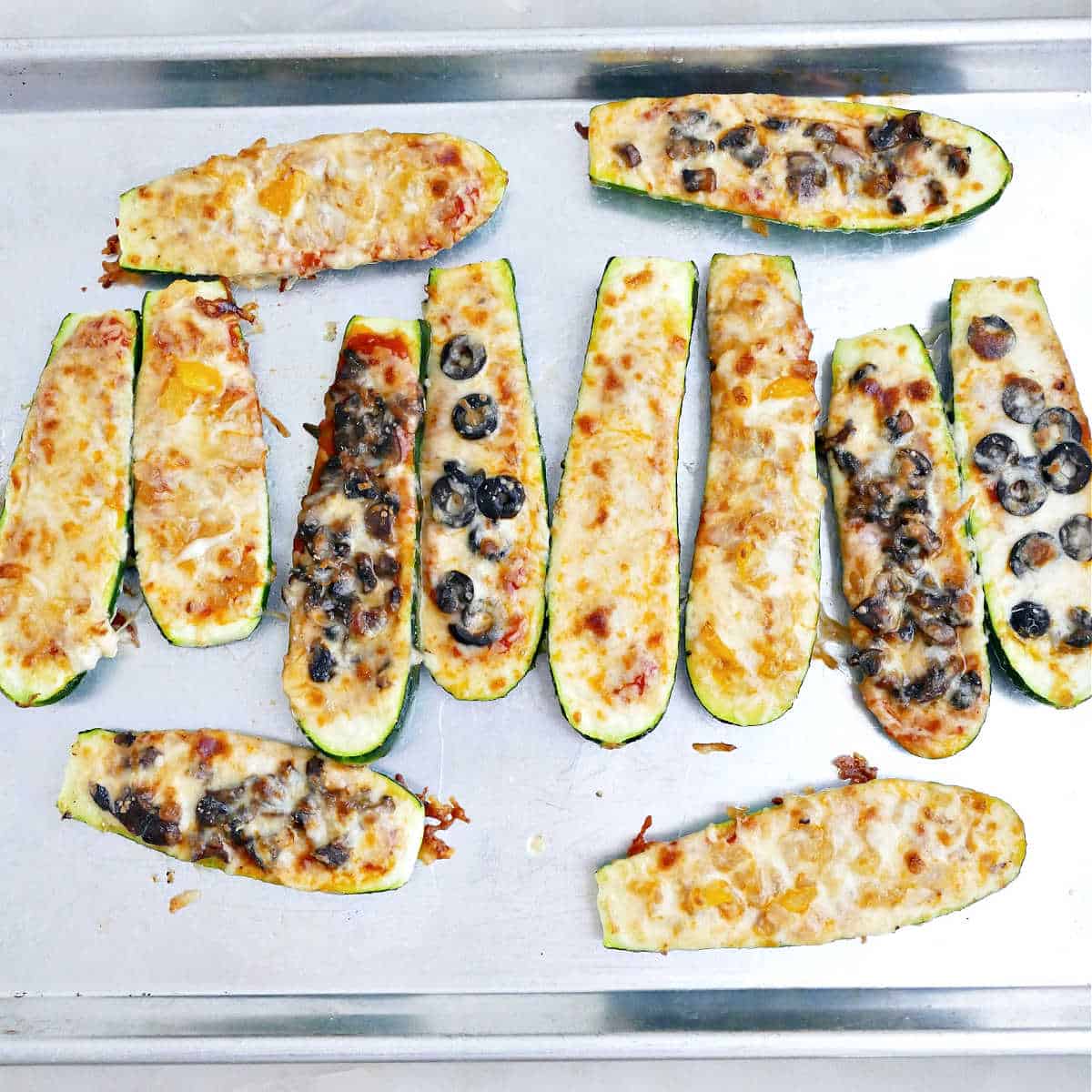 Zucchini pizza boats with toppings on a baking sheet after being baked.