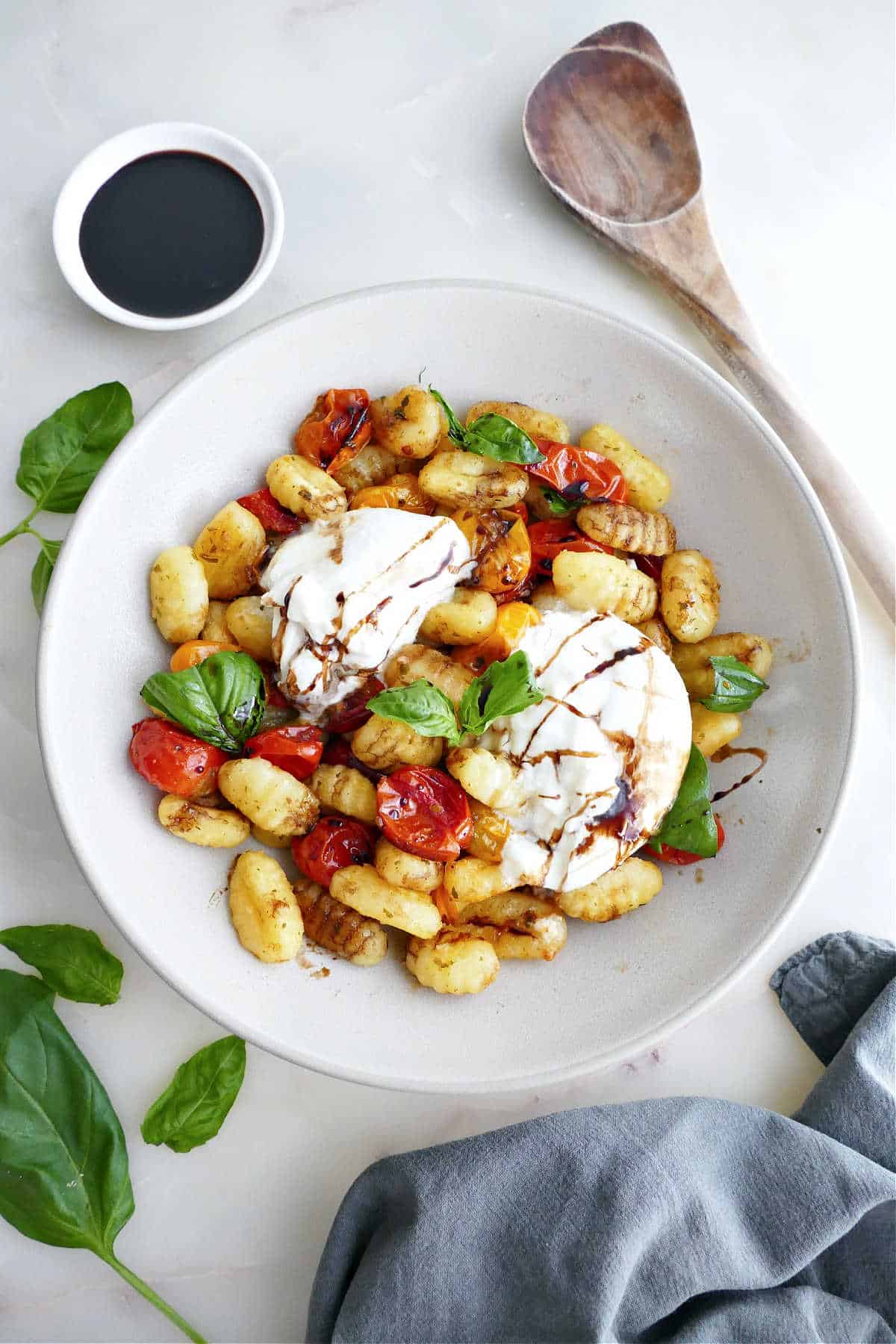 Roasted gnocchi and tomatoes with burrata, basil, and balsamic in a bowl.