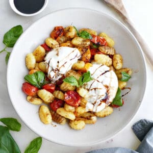 Roasted gnocchi and tomatoes with burrata, basil, and balsamic in a bowl.