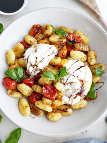 Roasted gnocchi and tomatoes with burrata, basil, and balsamic in a bowl.