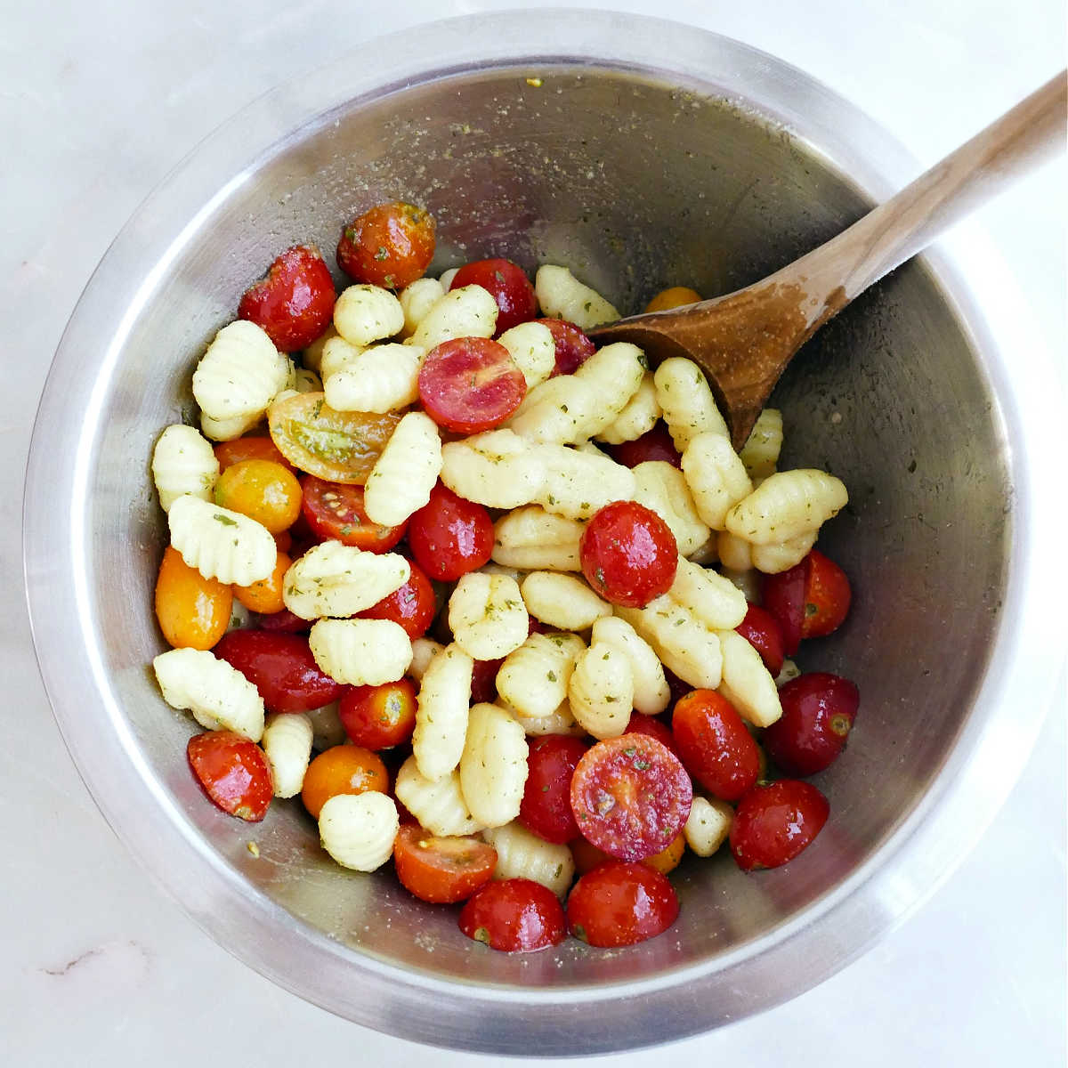 Gnocchi and cherry tomatoes being tossed with oil and seasonings in a bowl.