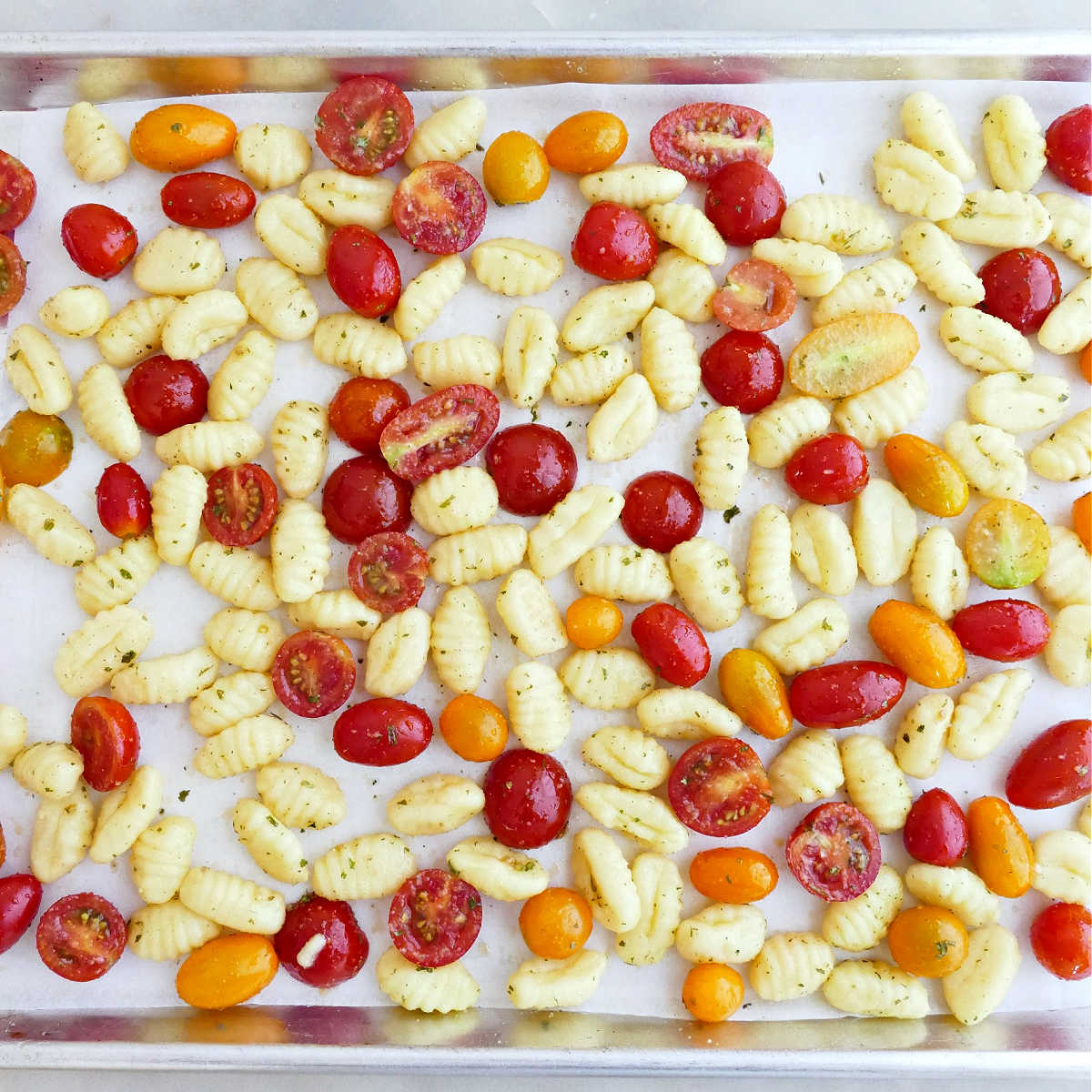 Gnocchi and tomatoes spread on a lined sheet pan before going in the oven.