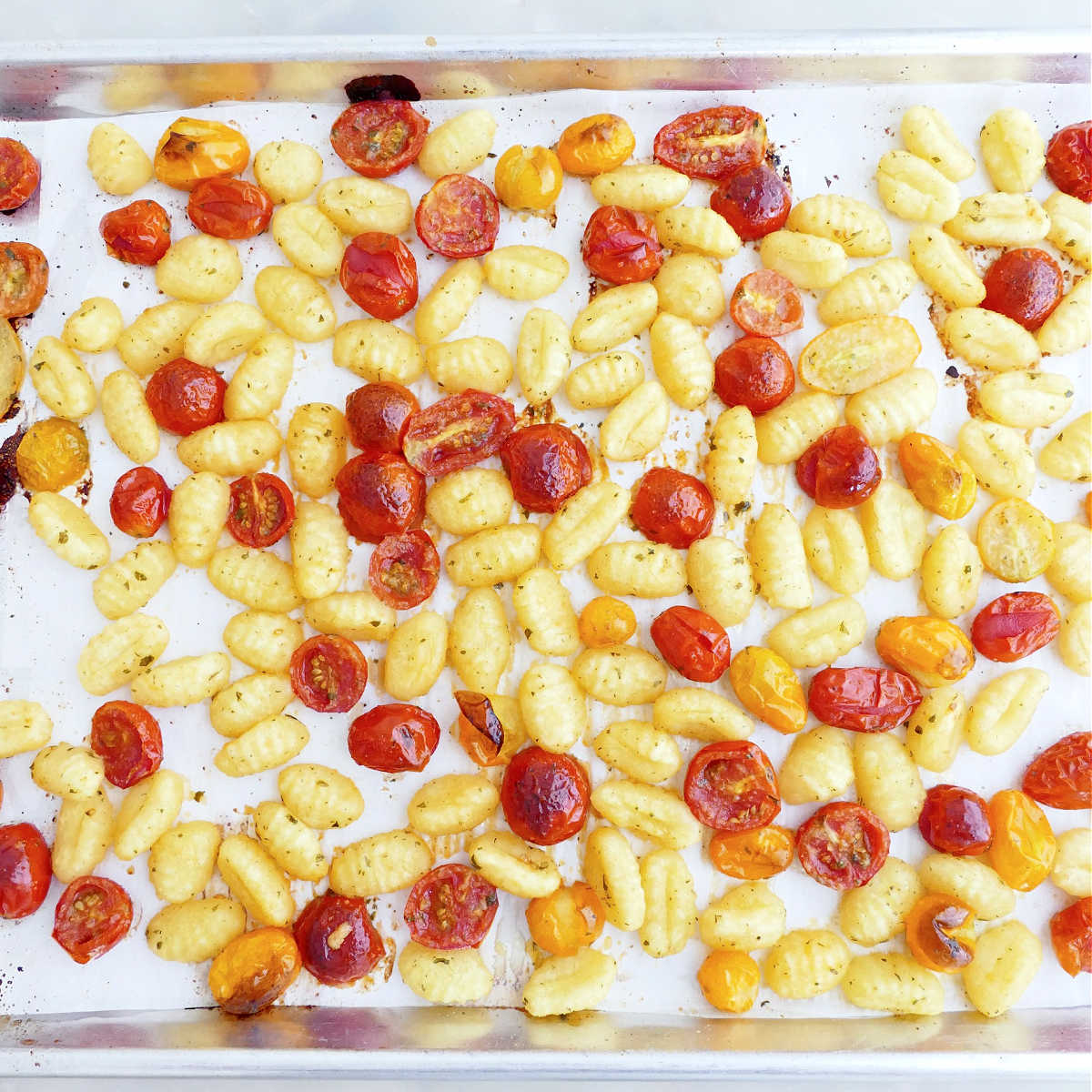 Gnocchi and tomatoes on a sheet pan after being roasted.